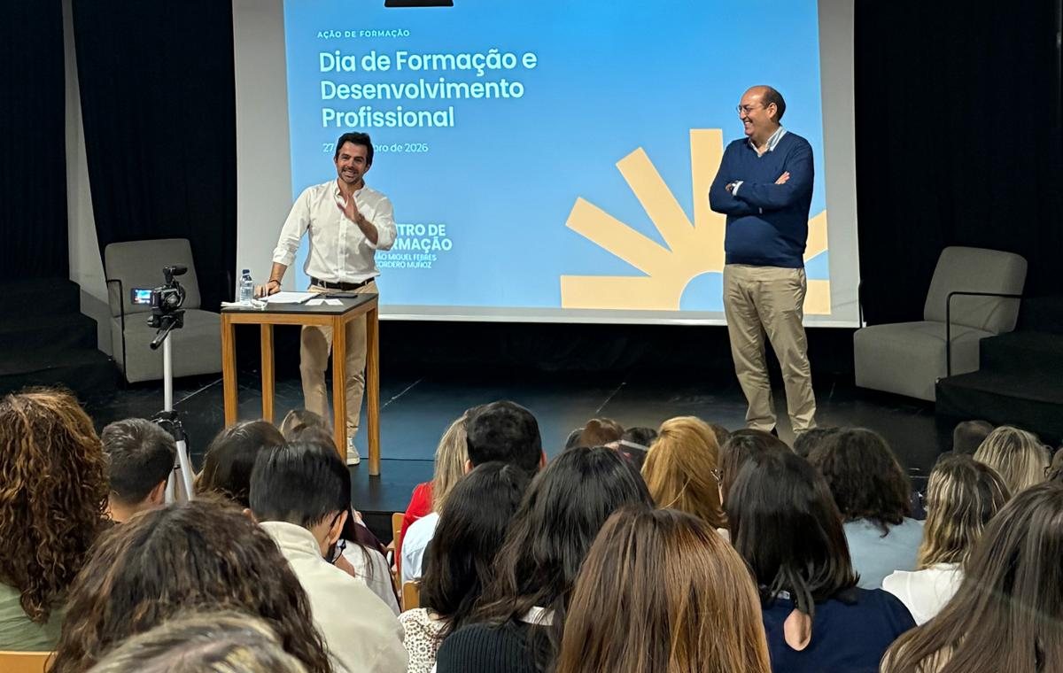Dois oradores no palco do auditório, diante do ecrã do Dia de Formação e Desenvolvimento Profissional, com o público em primeiro plano
