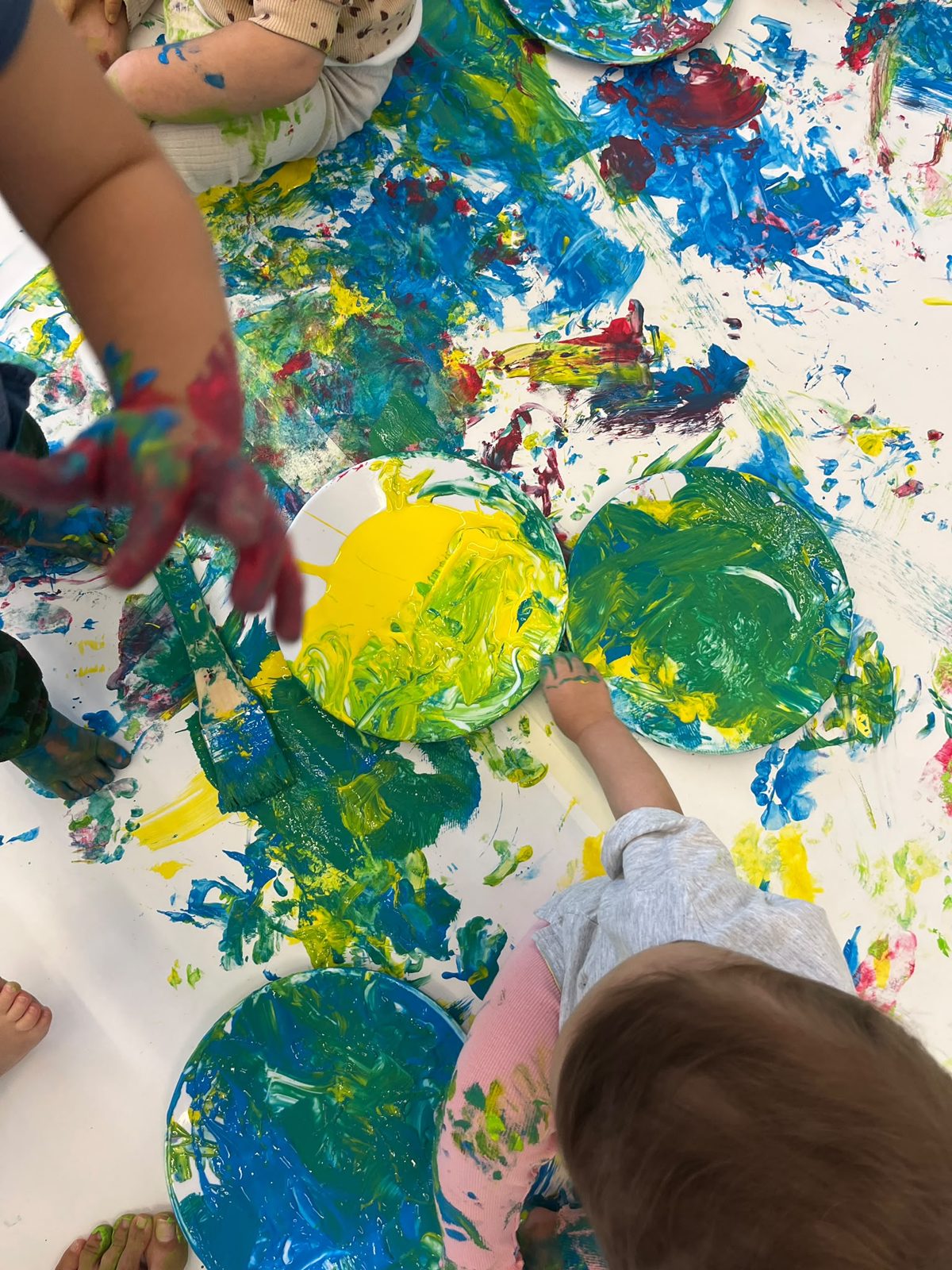 Crianças a pintar com as mãos à volta de pratos de tinta