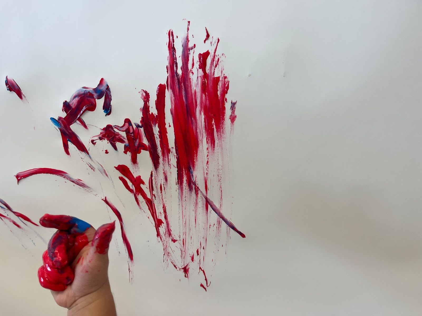 Mão de uma criança com tinta vermelha a pintar no papel