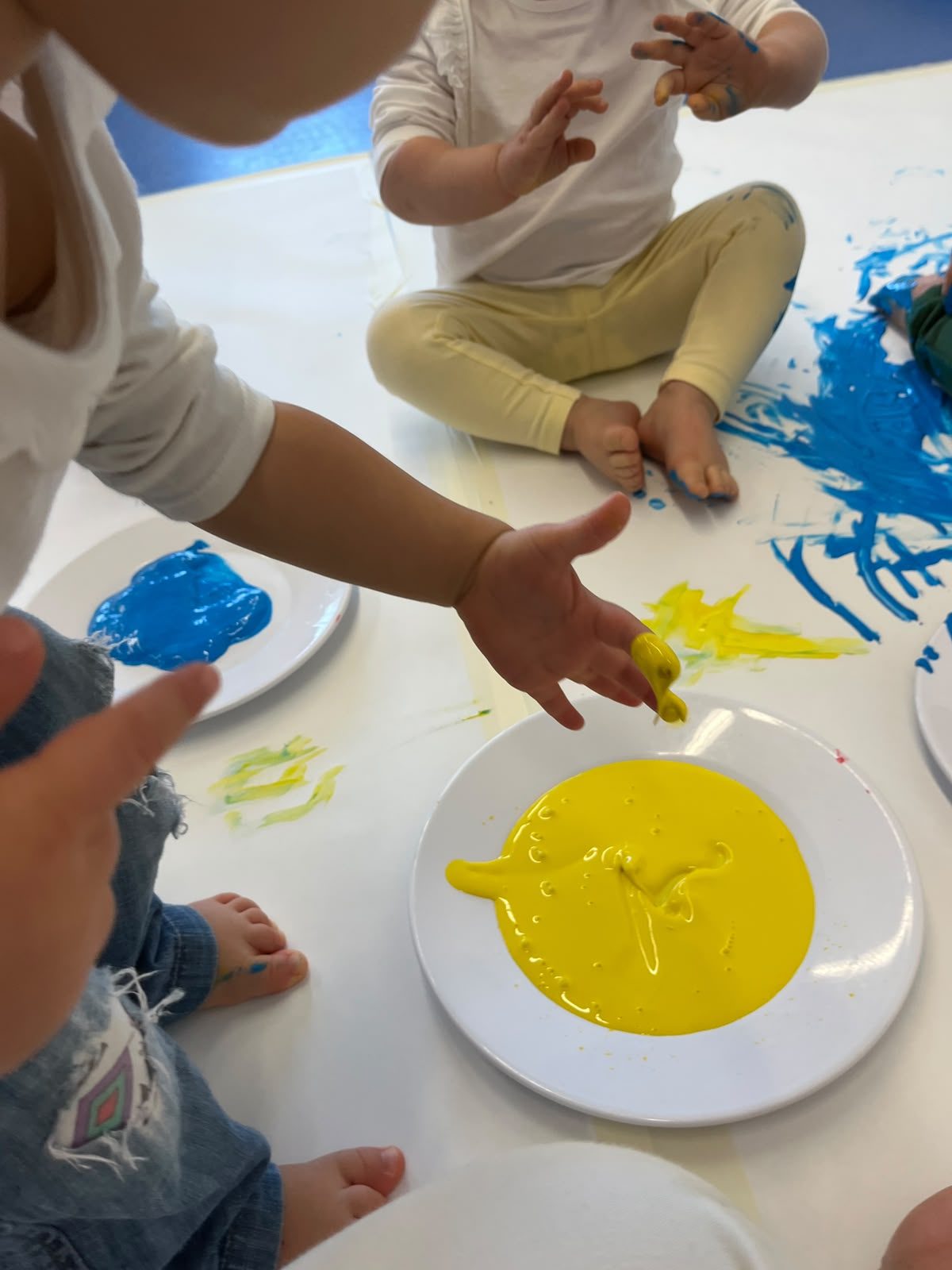 Crianças sentadas no papel de cenário, a pintar com as mãos