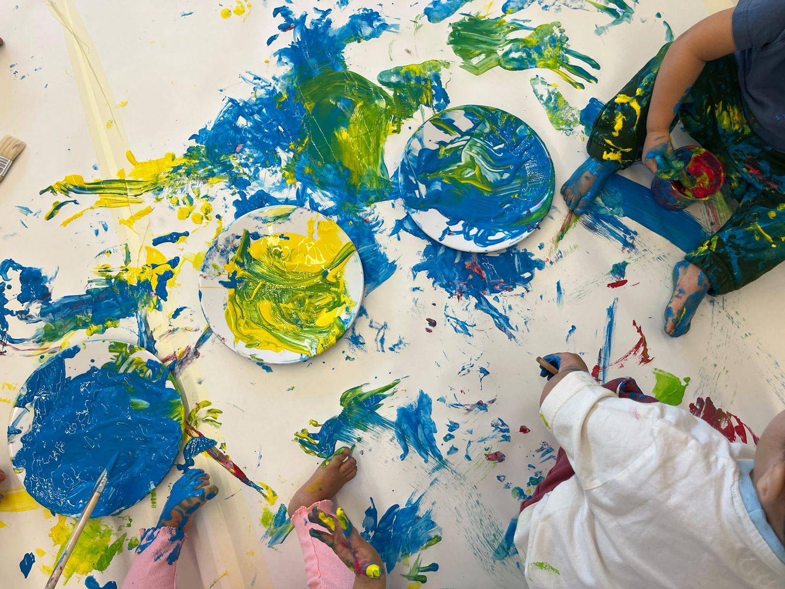 Pratos de tinta azul e amarela e marcas de mãos e pés no papel de cenário