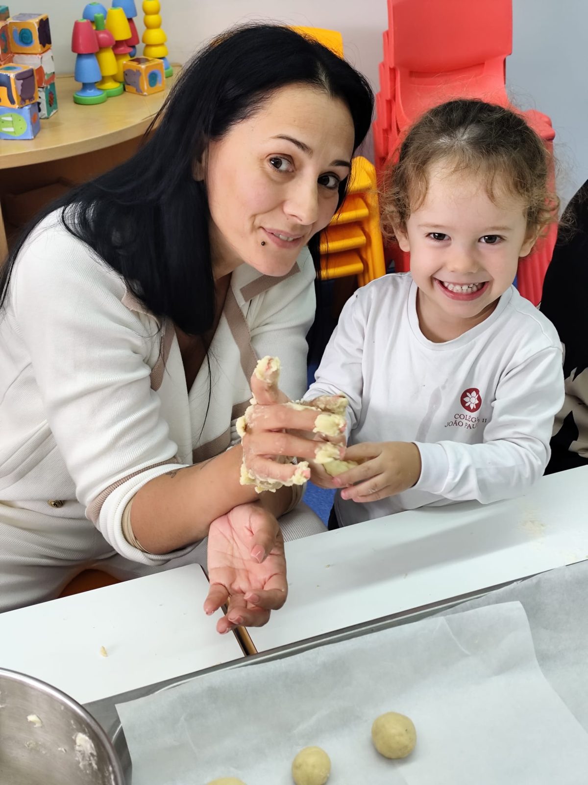 Uma mãe e a filha, sorridentes, a moldar a massa dos bolinhos do Pão por Deus
