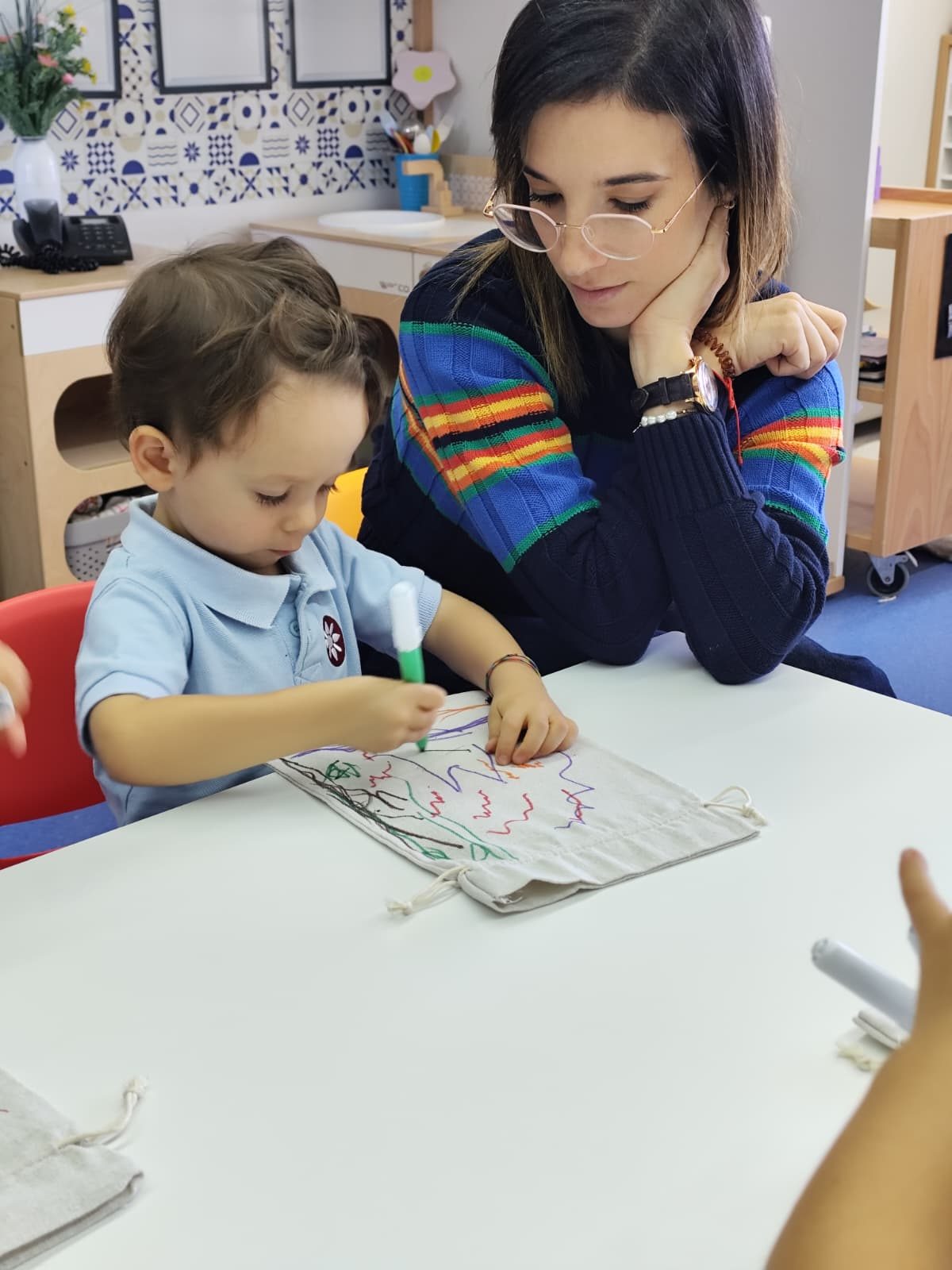 Criança a pintar o saquinho de pano, com a mãe a observar