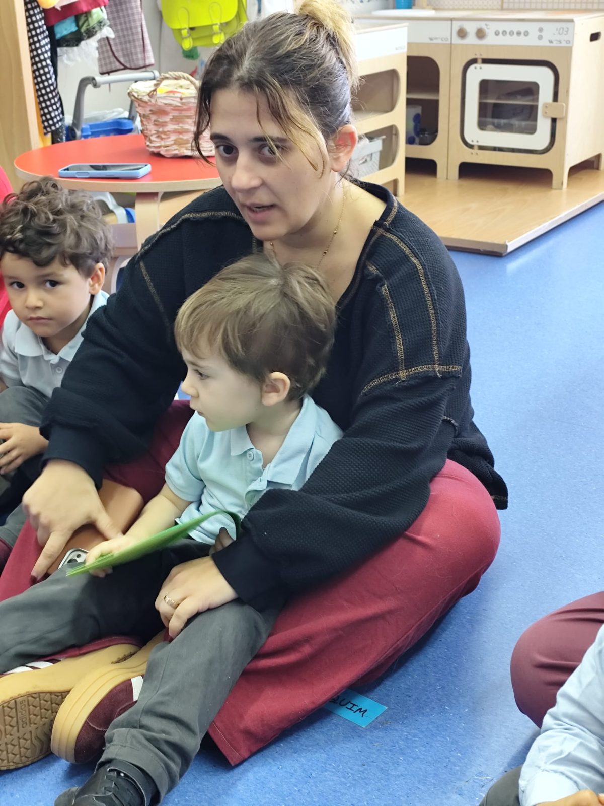Mãe sentada no chão com o filho ao colo, a contar a história ao grupo