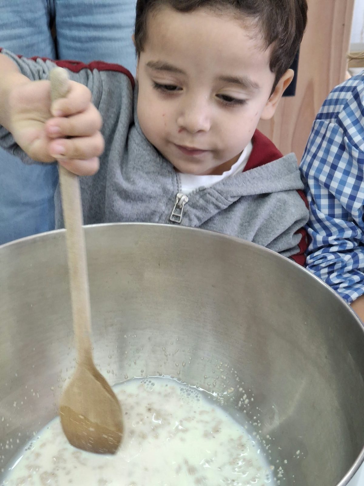 Criança a mexer a massa numa taça grande com uma colher de pau